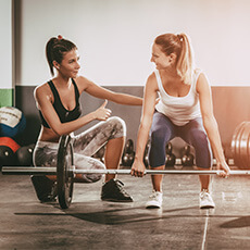 trainer helping woman lift barbell