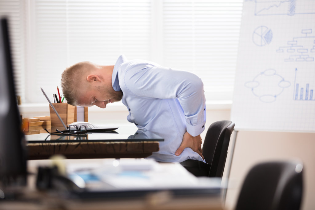 man clutching his back in pain at work desk