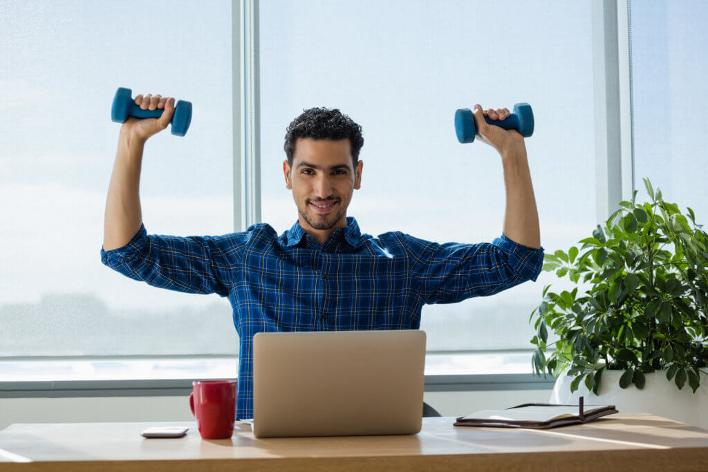 man sitting at desk doing a shoulder press with dumbbells