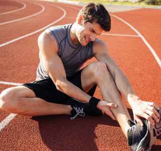 man sitting in ground in pain with sore muscles