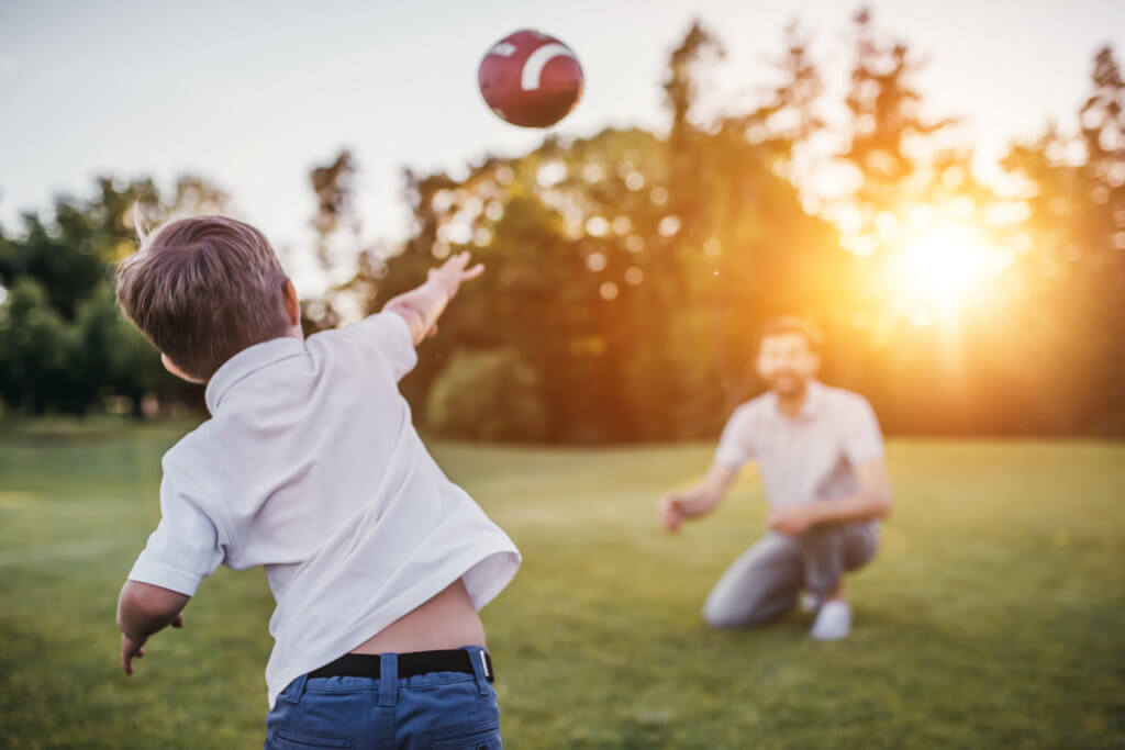 son and father playing catch with a football