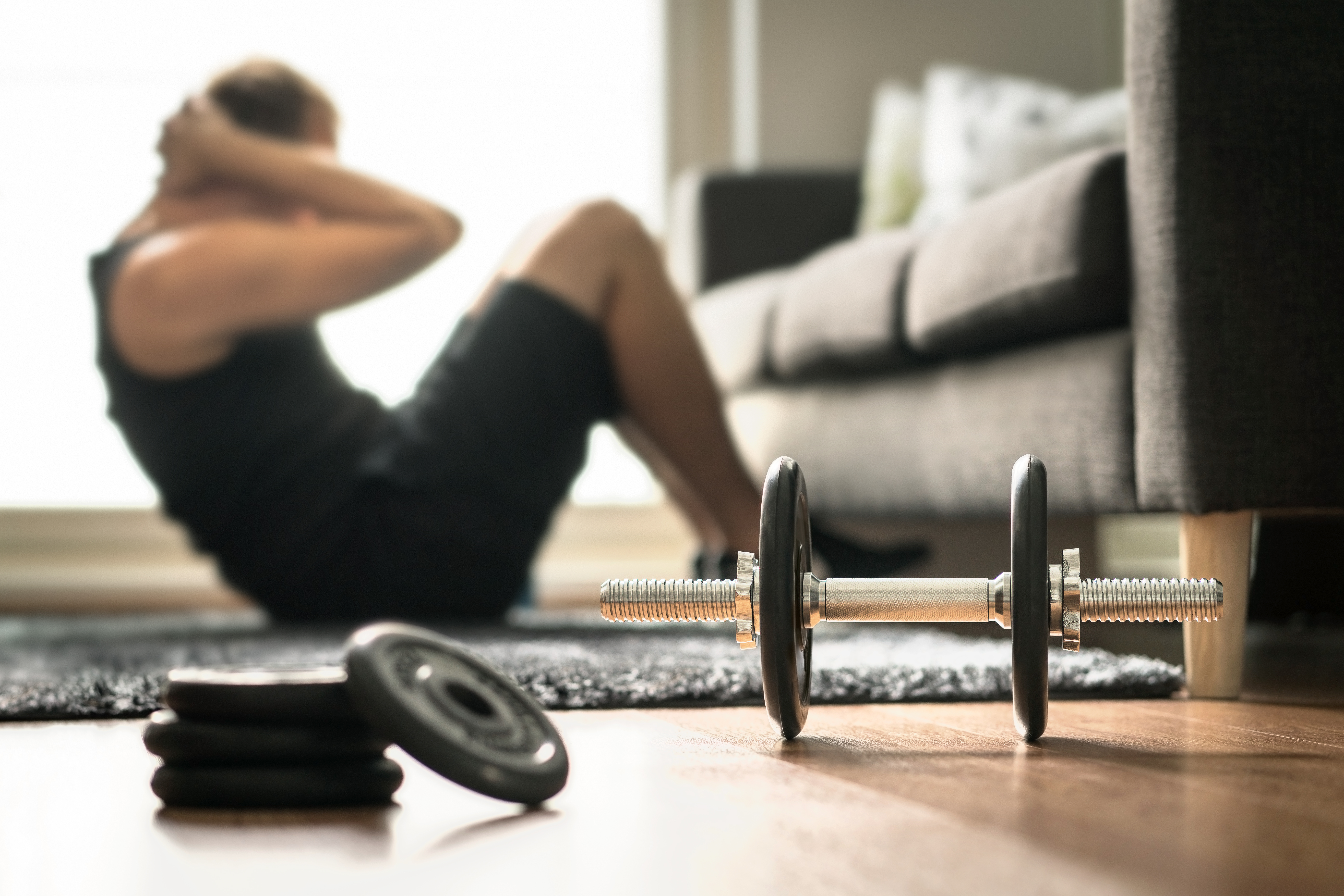 man doing sit up in living room next to dumbbell