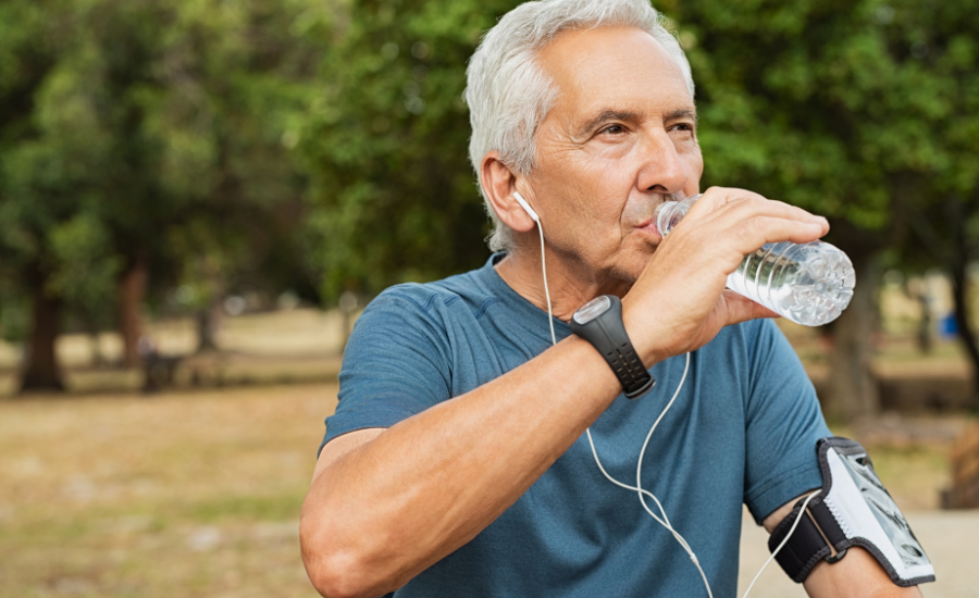 Man wearing earbuds and drinking water outside.